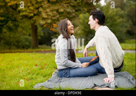 Young couple on blanket in park, laughing Stock Photo