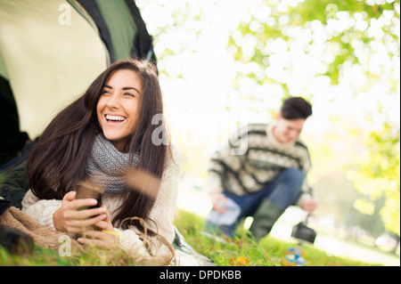 Young woman in tent using smartphone, laughing Stock Photo