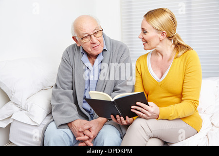 Woman reading a book to a senior citizen man in nursing home Stock Photo