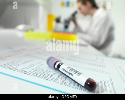 Blood tube sitting on blood results with technician at microscope in lab Stock Photo