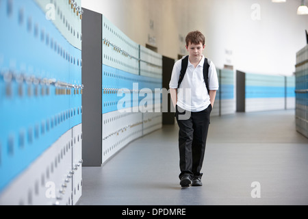 Unhappy schoolboy walking alone in school corridor Stock Photo