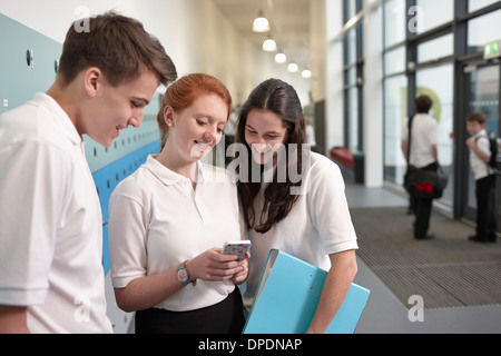 Teenagers looking at mobile phone in school corridor Stock Photo