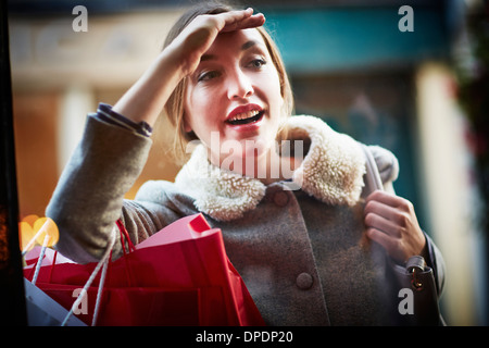 Young woman carrying shopping bag, looking through window Stock Photo