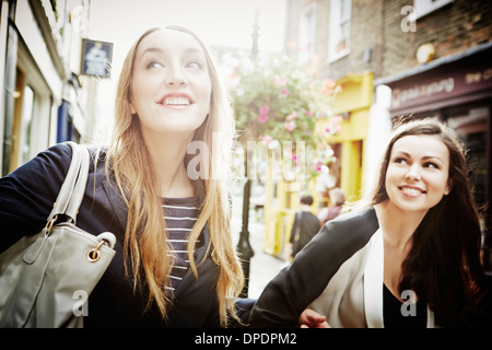 Young women walking down street carrying bags and laughing Stock Photo