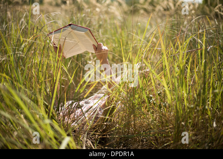 Woman lying in long grass reading book Stock Photo