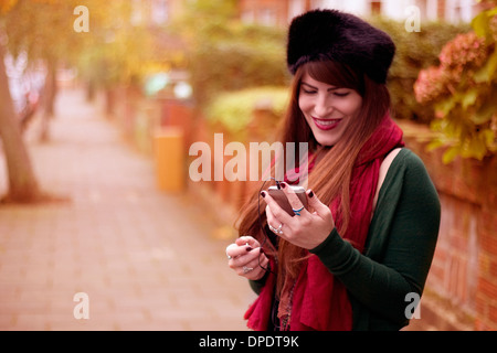 Young woman wearing winter clothing, holding smartphone Stock Photo