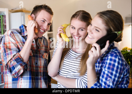 Three young people having fun using fruit as telephones Stock Photo