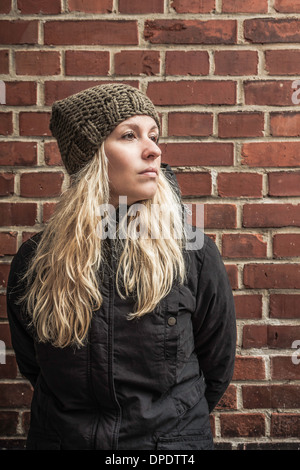Portrait of young woman by brick wall wearing knit hat Stock Photo