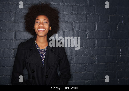 Young woman by black brick wall wearing black jacket Stock Photo