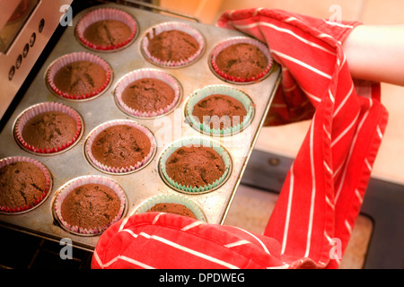 Close up of hands removing cupcakes from oven Stock Photo