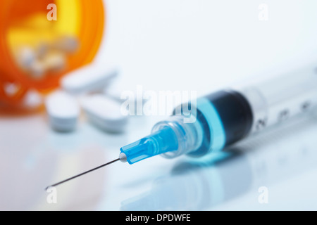 Disposable plastic medical syringe with attached hypodermic needle. Pill bottle and pills in the background Stock Photo