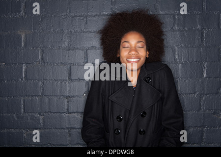 Young woman by black brick wall wearing black jacket Stock Photo