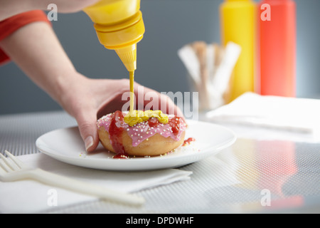 Woman squirting donut with ketchup and mustard Stock Photo