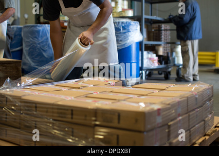 Factory worker wrapping cardboard boxes with clingfilm Stock Photo