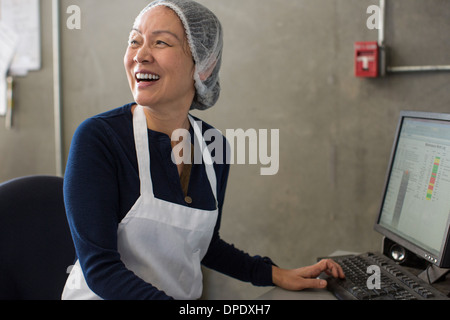 Woman wearing apron and hairnet using computer Stock Photo