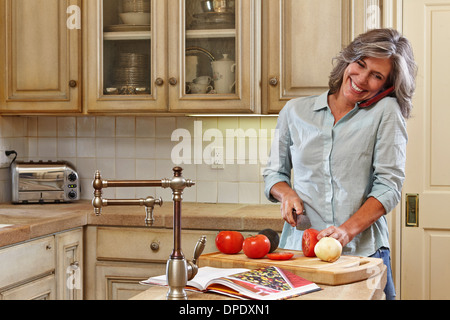 Mature woman using mobile and preparing food in kitchen Stock Photo