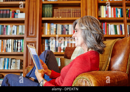 Mature woman sitting in home study using digital tablet Stock Photo