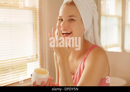 Young woman in bathroom putting on face cream