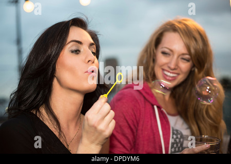 Two female friends blowing bubbles at rooftop party Stock Photo
