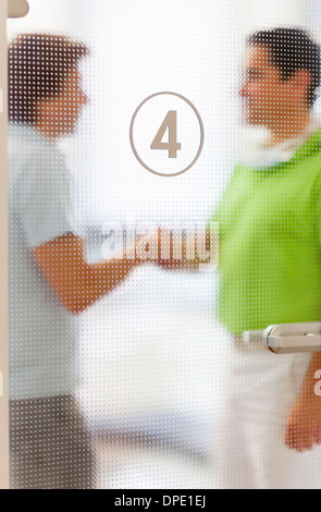Two men shaking hands behind glass door Stock Photo
