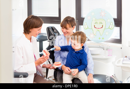 Dentist teaching boy on mothers lap how to brush teeth Stock Photo