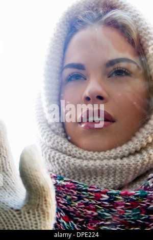 Portrait of young woman wrapped up looking through window