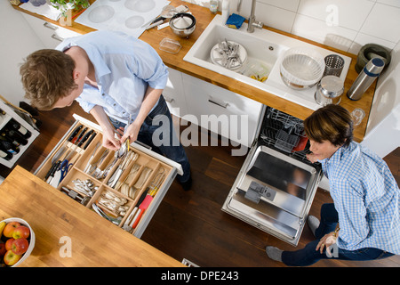 Grandmother and adult grandson tidying away cutlery from dishwasher Stock Photo