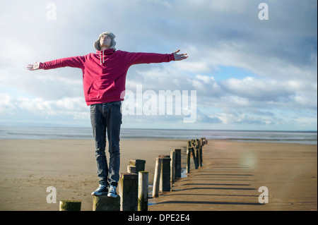 Young man standing on groynes, Brean Sands, Somerset, England Stock Photo