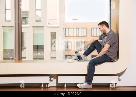 Businessman sitting on windowsill using laptop Stock Photo