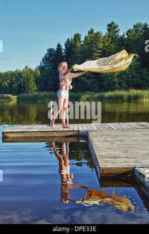 Young woman shaking blanket on pier, Gavle, Sweden Stock Photo