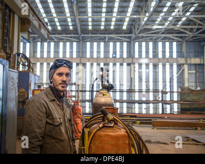 Portrait of welder wearing overalls and safety goggles in factory