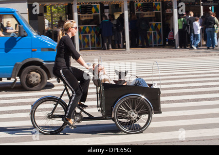 Denmark, Copenhagen, young woman riding a Christiania bike with man and dog as passengers Stock Photo