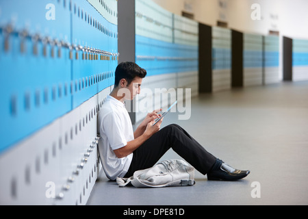Portrait of teenage schoolboy sitting on floor next to lockers