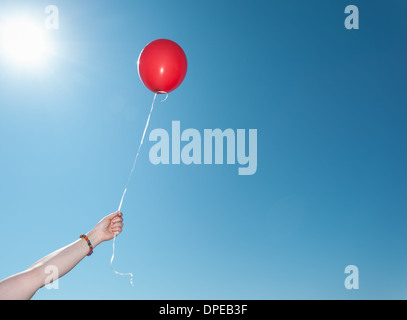 Hand holding single red balloon against blue sky Stock Photo