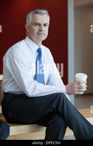 Businessman in waiting area of office, with hot drink Stock Photo