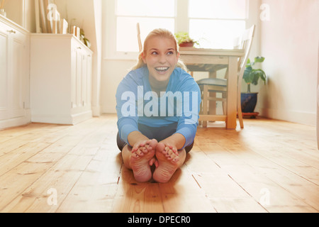 Young woman sitting on floor leaning forwards touching toes Stock Photo