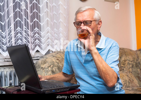 Senior man using laptop and drinking whiskey at home. Stock Photo