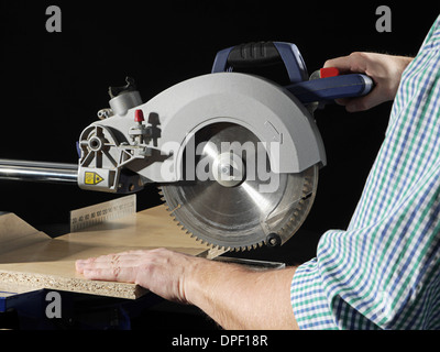 Carpenter cutting flaxboard using sliding compound mitre saw Stock Photo