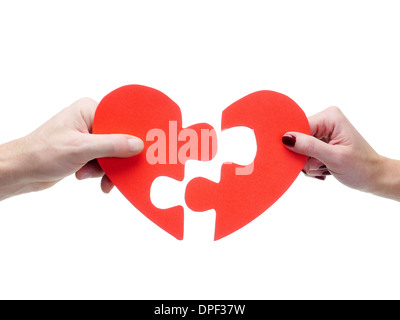 Male and female hand matching red jigsaw heart halves over white background Stock Photo