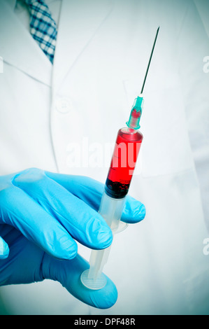 a doctor wearing medical gloves holding a syringe with blood Stock Photo