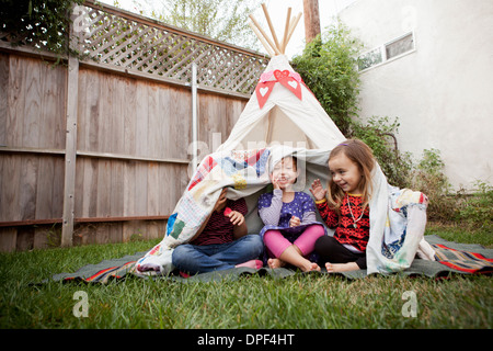 Three young girls in garden hiding under blanket Stock Photo