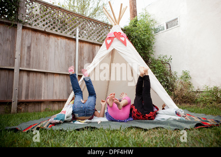Three young girls in garden with legs raised Stock Photo