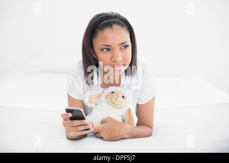 Thoughtful young dark haired model holding a mobile phone and a plush sheep Stock Photo