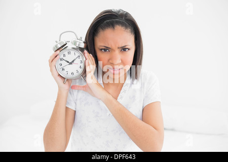 Frowning young dark haired model holding an alarm clock Stock Photo