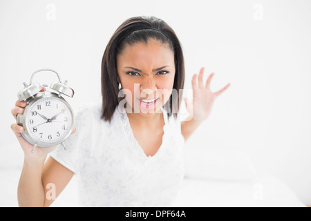 Furious young dark haired model throwing an alarm clock Stock Photo