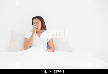 Exhausted young dark haired model yawning lying in her bed Stock Photo
