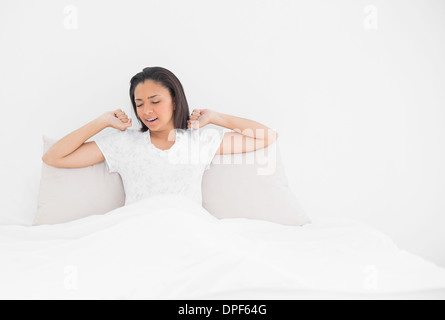 Tired young dark haired model stretching in her bed Stock Photo