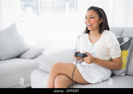 Laughing young dark haired woman in white clothes playing video games Stock Photo