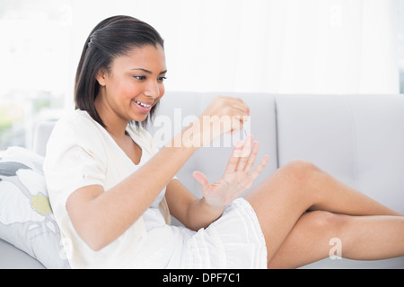 Charming young dark haired woman in white clothes applying nail polish Stock Photo