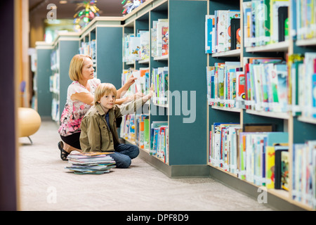 Boy With Teacher Selecting Books From Bookshelf Stock Photo